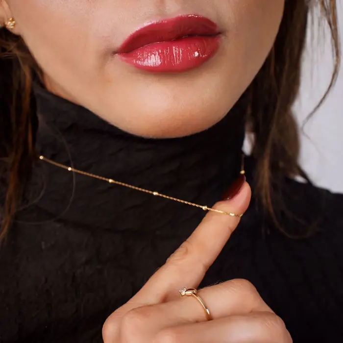 Detalhe de batom vermelho, colar e anel dourados numa modelo